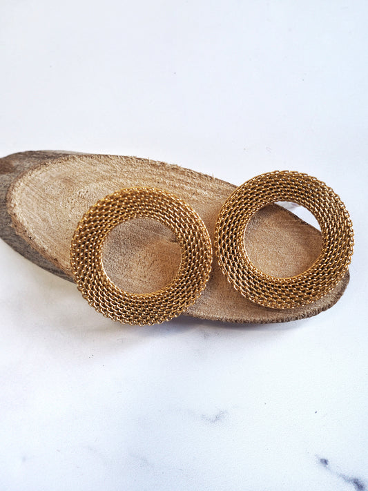 Pair of gold hoop earrings on a wooden stand with a marble background