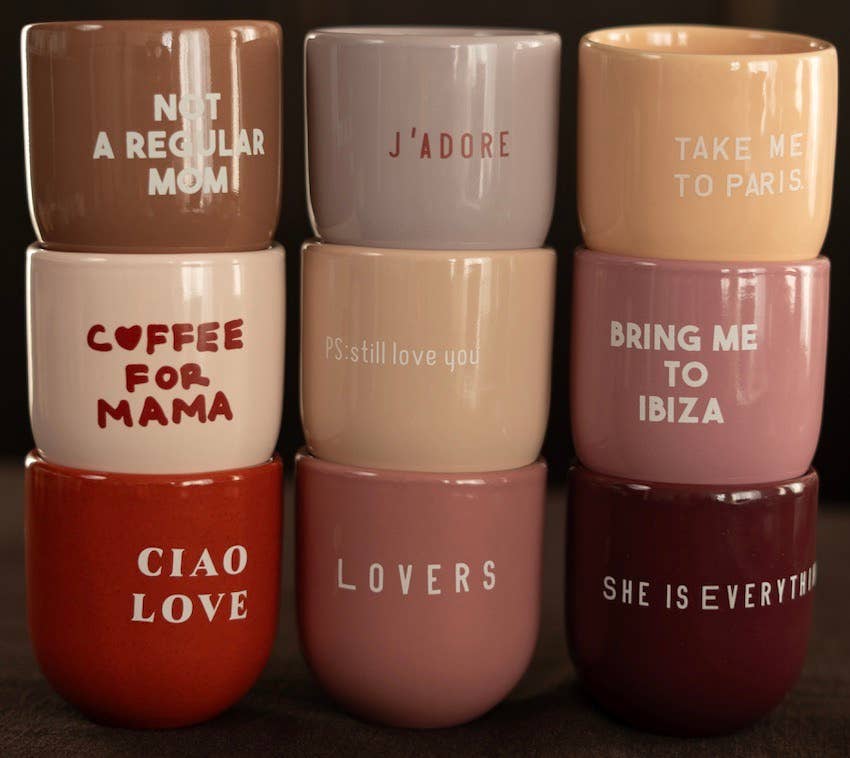 Stack of colorful mugs with various phrases printed on them against a dark background.