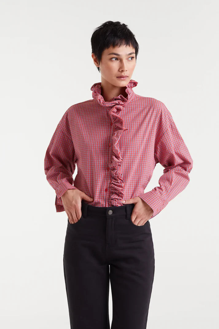 Person wearing a red checkered blouse with ruffled details on a white background