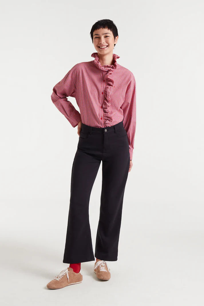 Person wearing a pink ruffled shirt and black pants on a white background