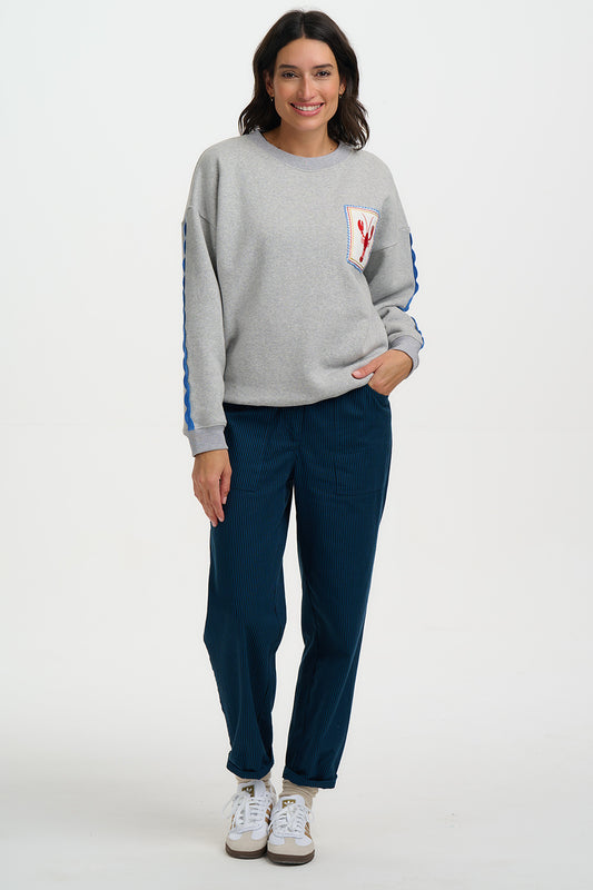Woman wearing a gray sweatshirt with a logo and blue pants on a white background