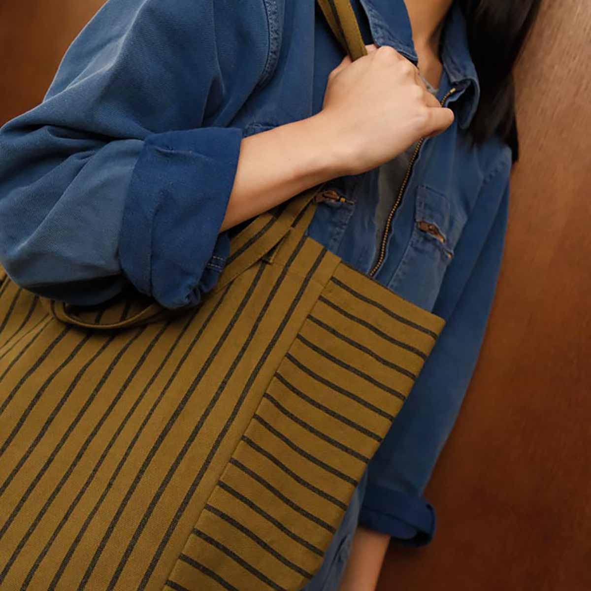Person wearing a blue jacket over a striped garment with a wooden background
