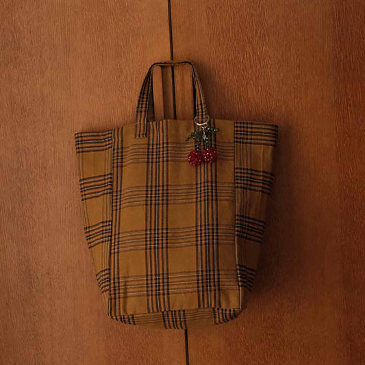 Plaid patterned bag with cherry charm on a wooden surface