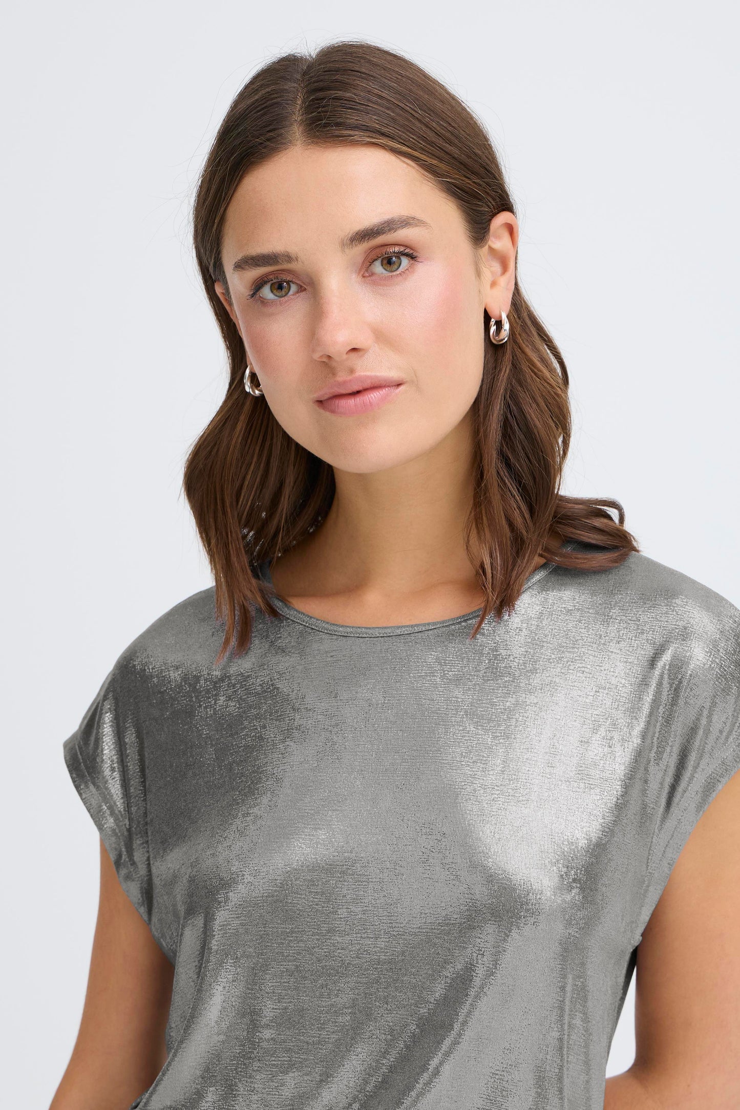 Woman wearing a silver metallic top against a plain background