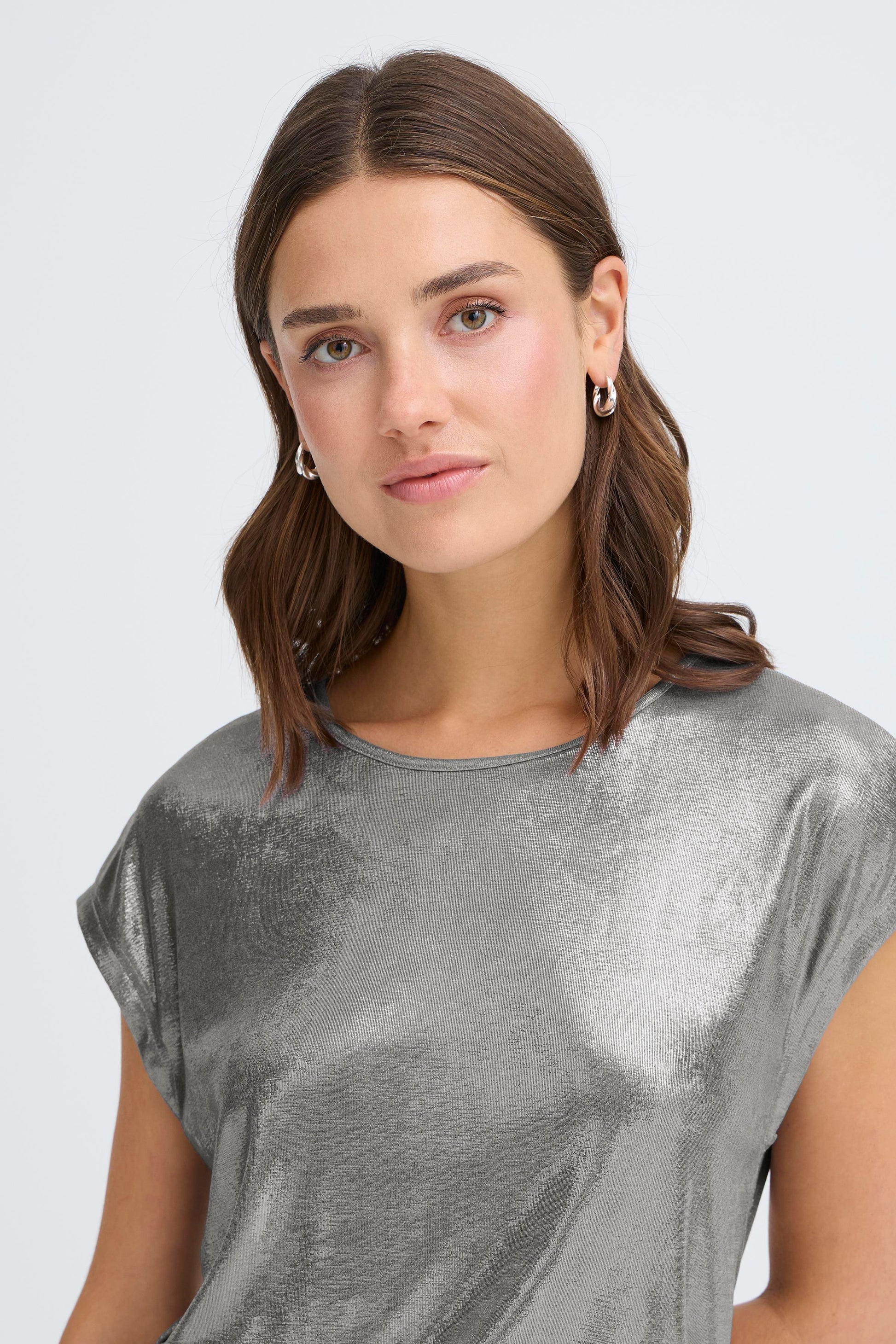 Woman wearing a silver metallic top against a plain background
