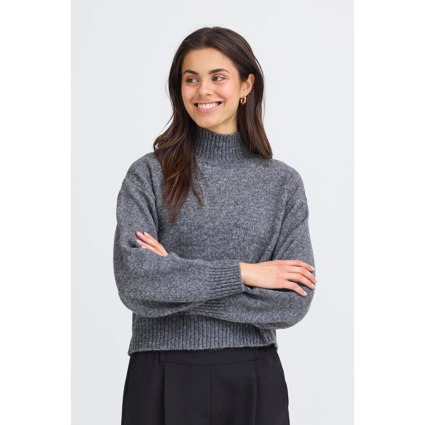 Woman wearing a gray sweater with arms crossed on a white background