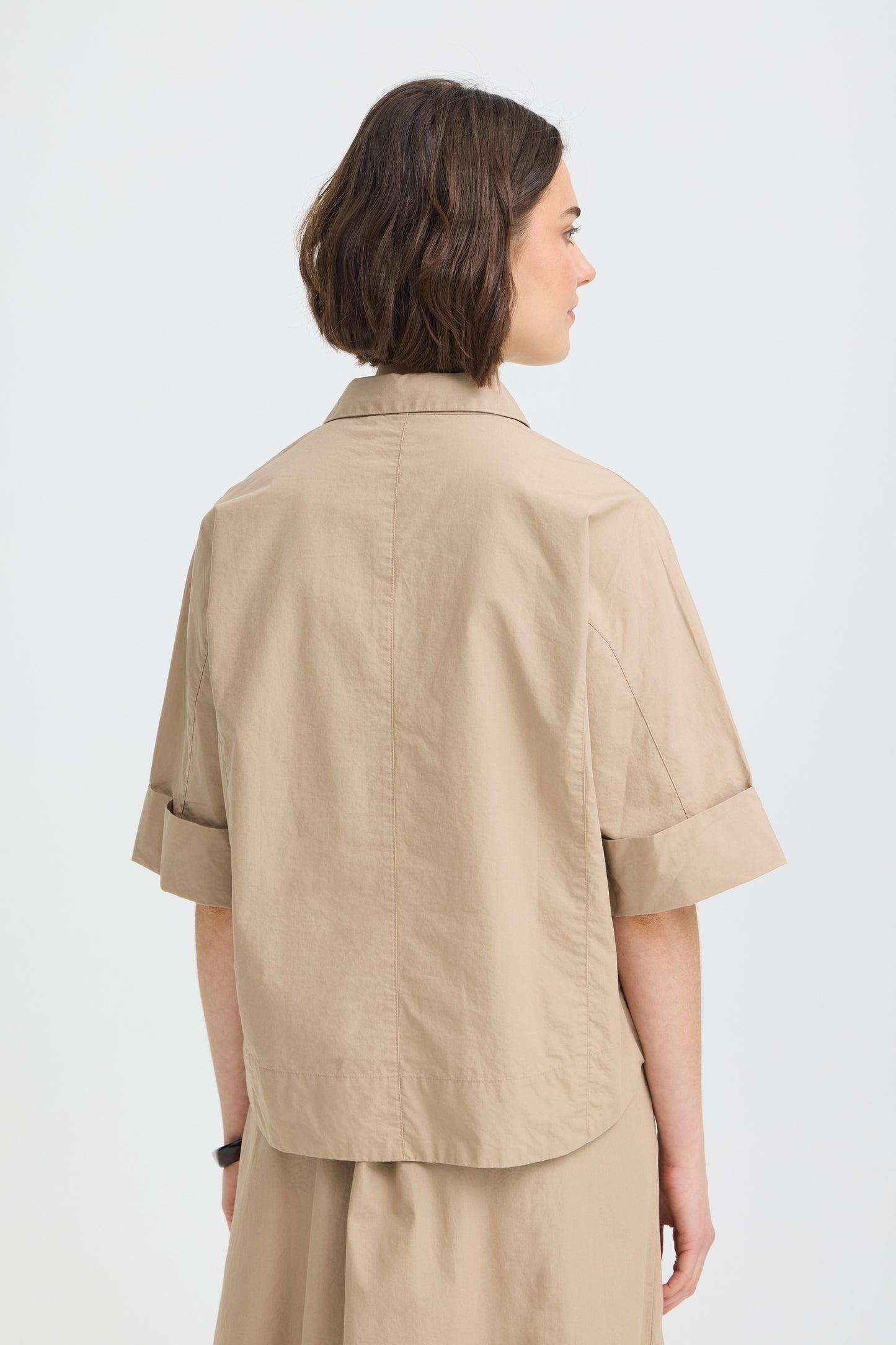 Person wearing a beige shirt and pants on a white background