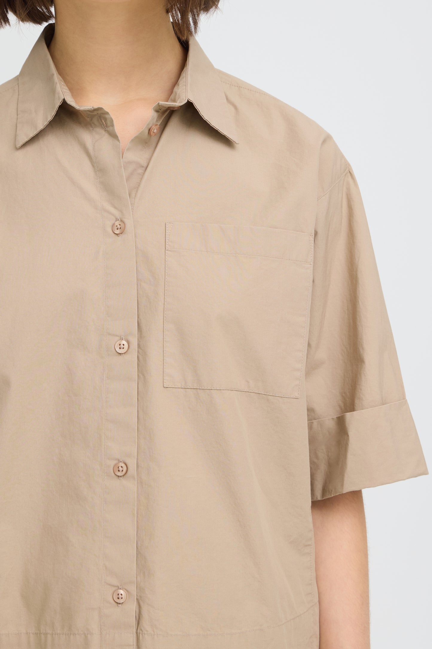 Beige short-sleeve shirt worn by a person on a light gray background