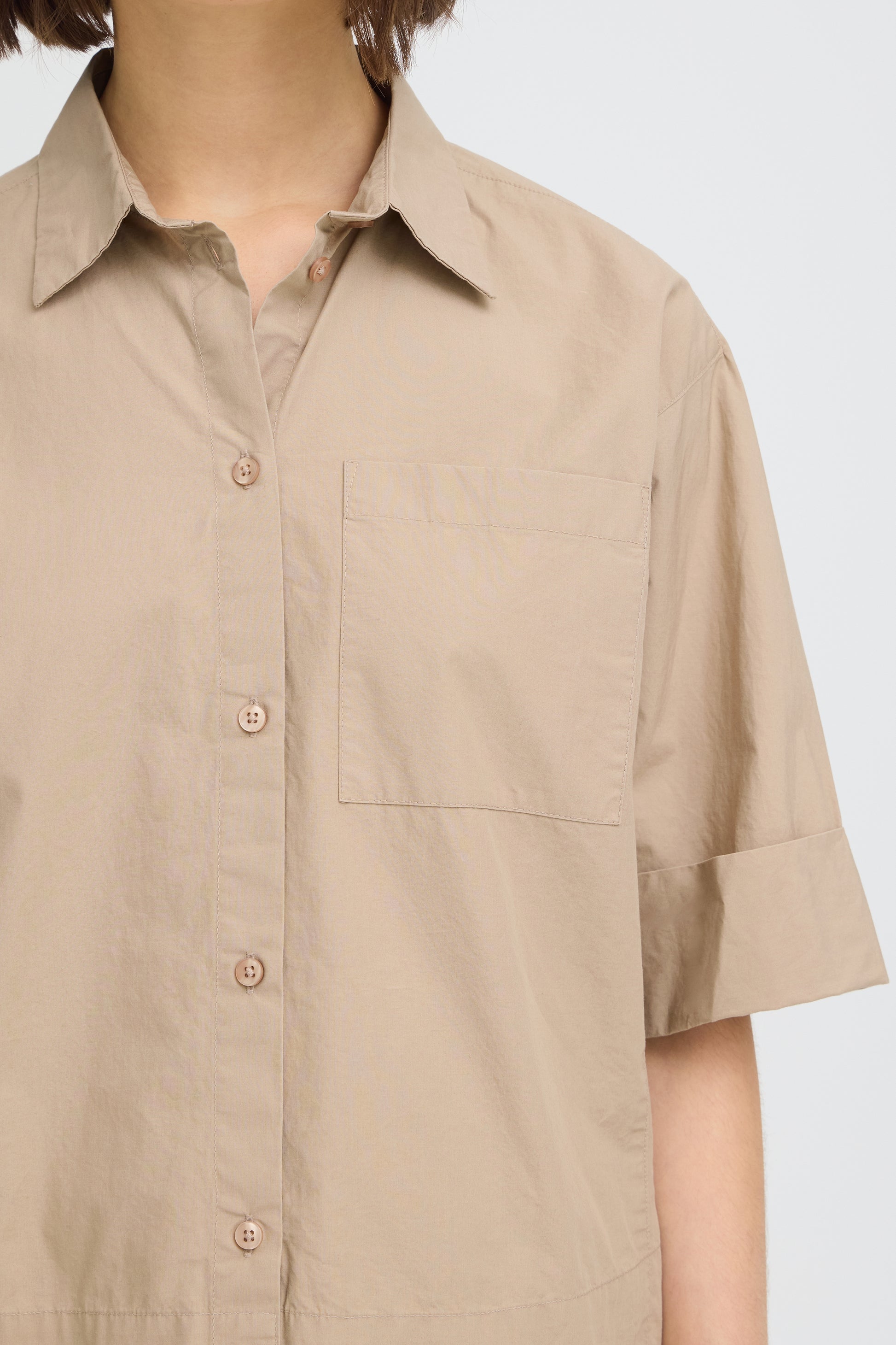 Beige short-sleeve shirt worn by a person on a light gray background