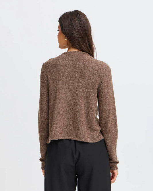 Person wearing a brown sweater and black pants on a light gray background