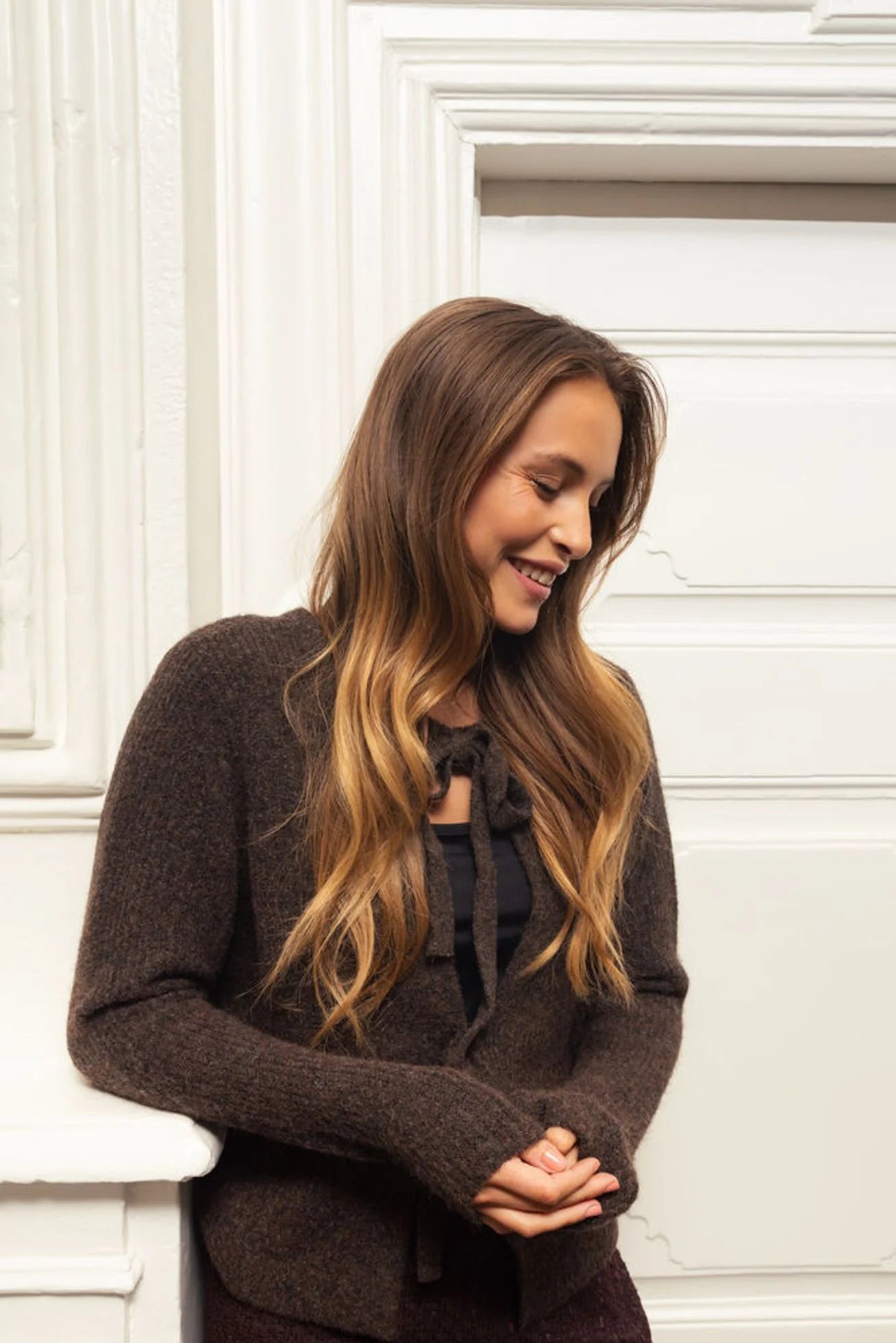 Woman wearing a brown sweater against a white wall