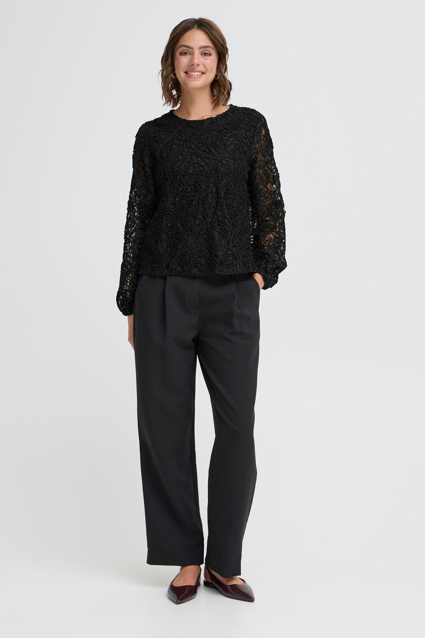 Woman wearing a black lace top and black pants on a white background