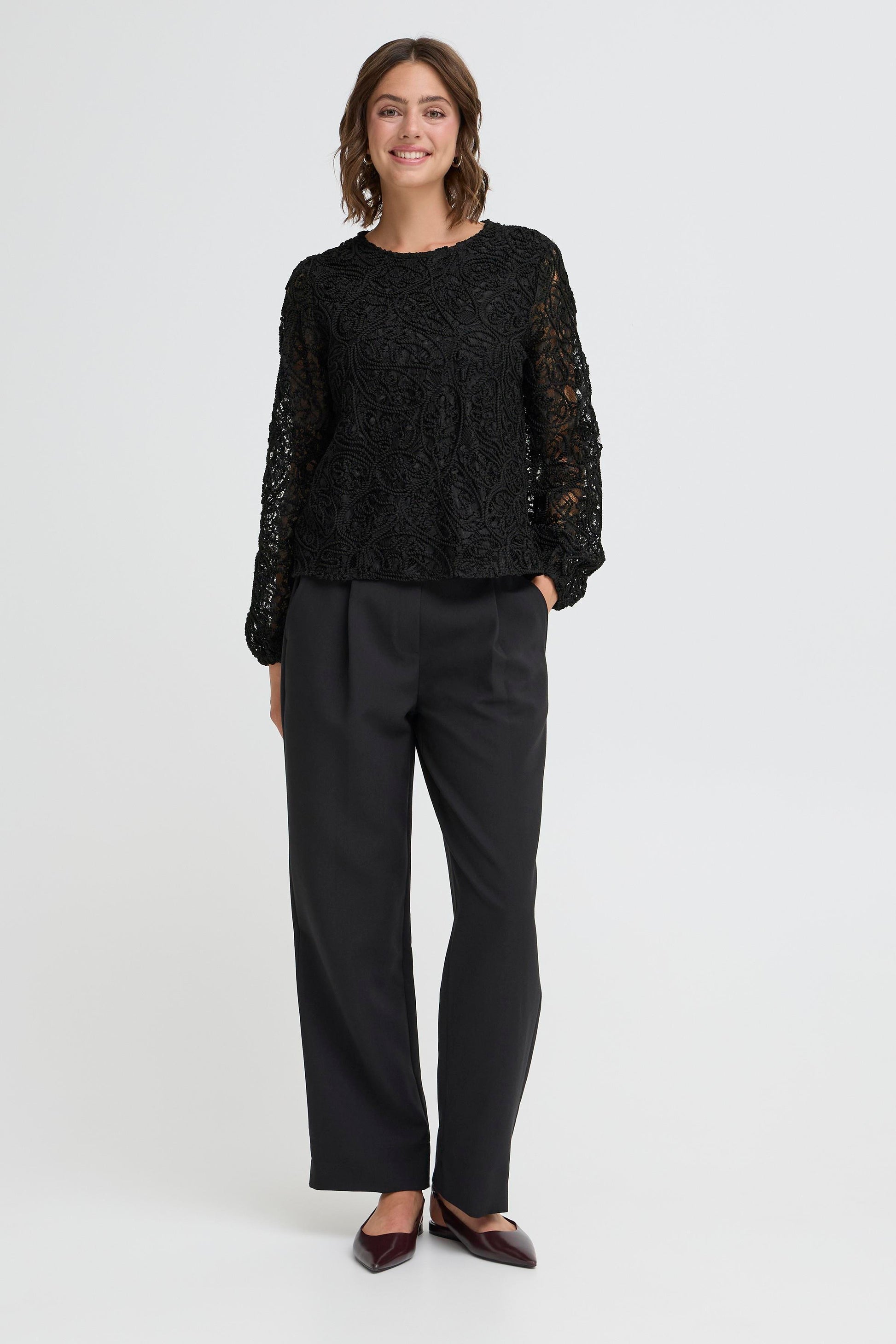Woman wearing a black lace top and black pants on a white background