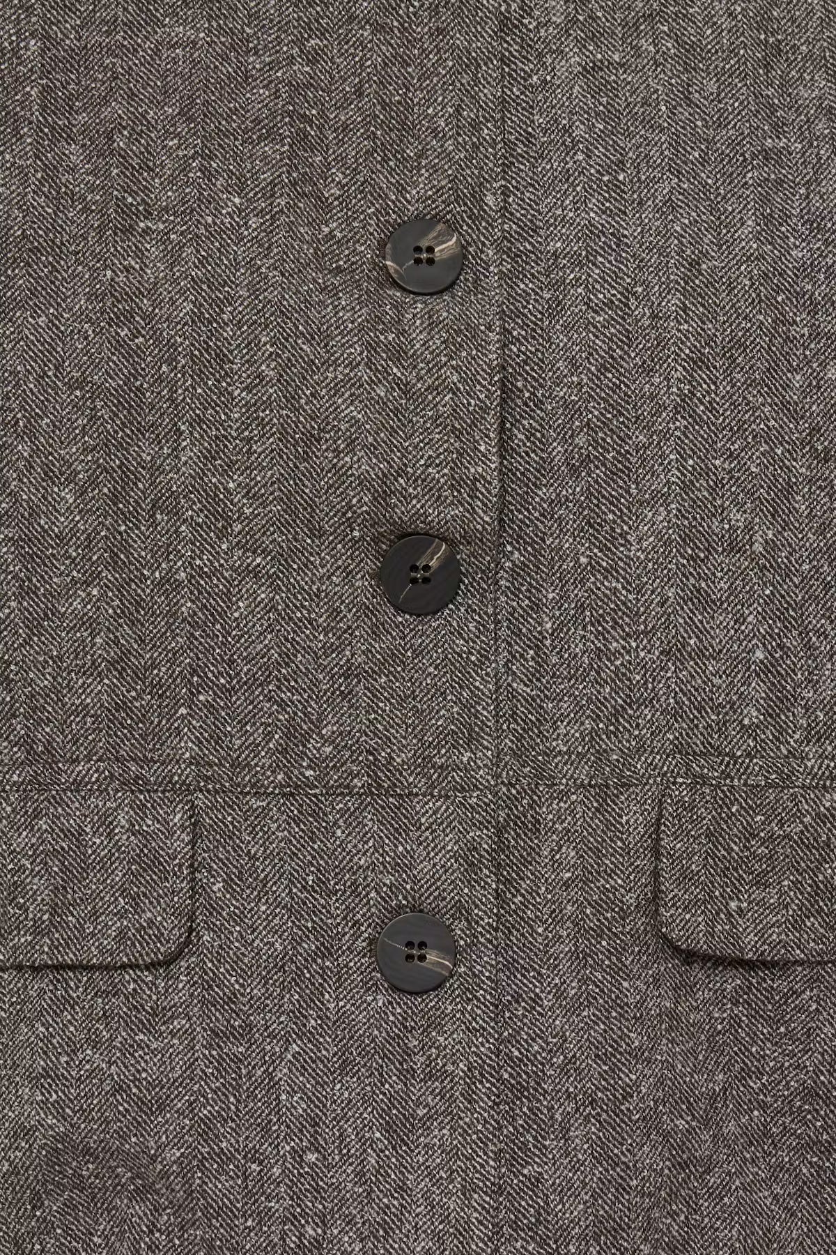 Close-up of a dark gray herringbone tweed fabric with three dark buttons and flap pockets on the sides.