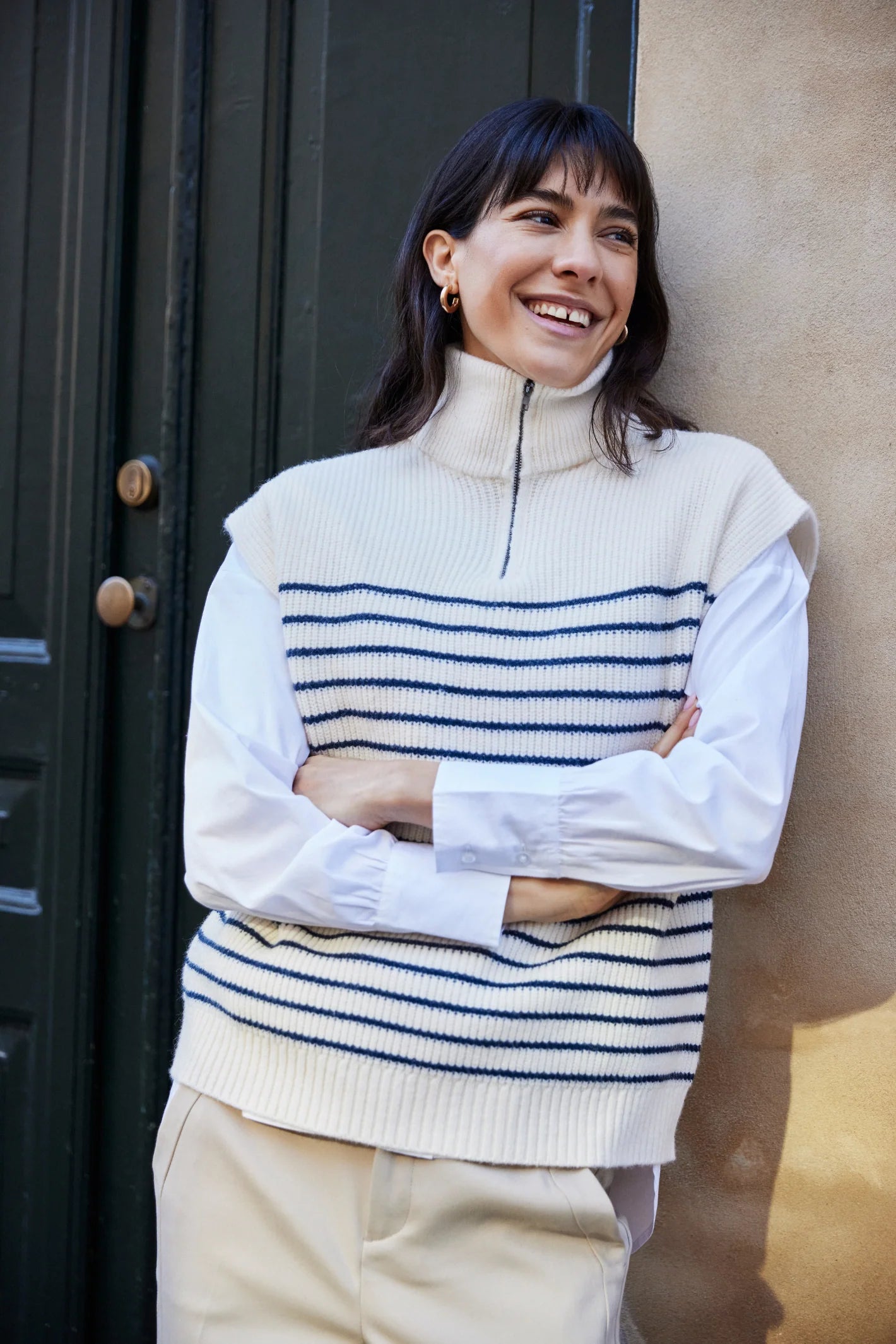 Woman wearing a striped sweater standing against a wall.