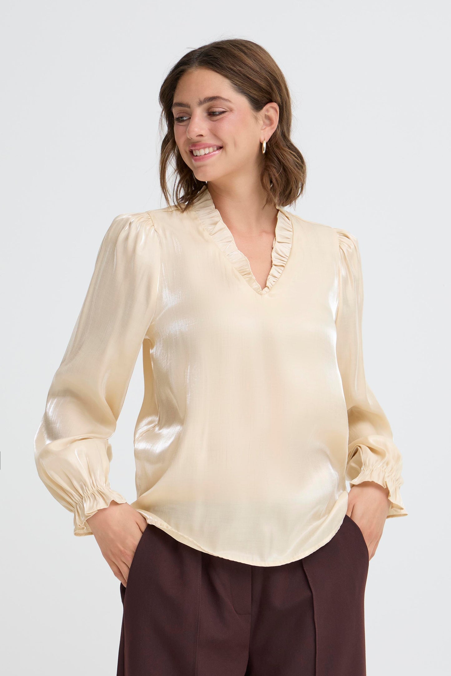Woman wearing a beige blouse with ruffled details on a white background