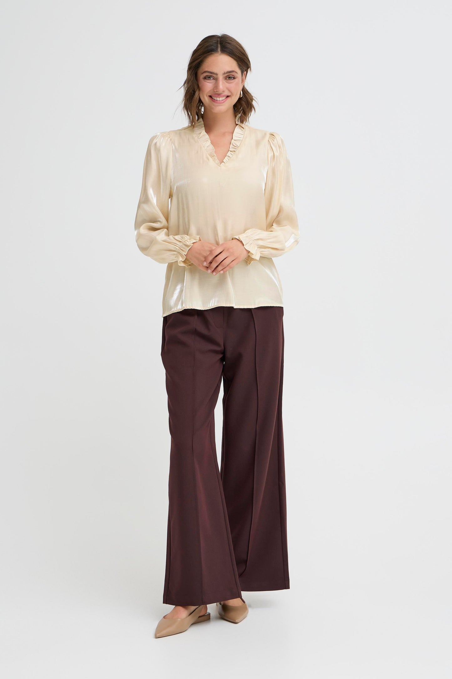 Woman wearing a beige blouse and brown pants on a white background