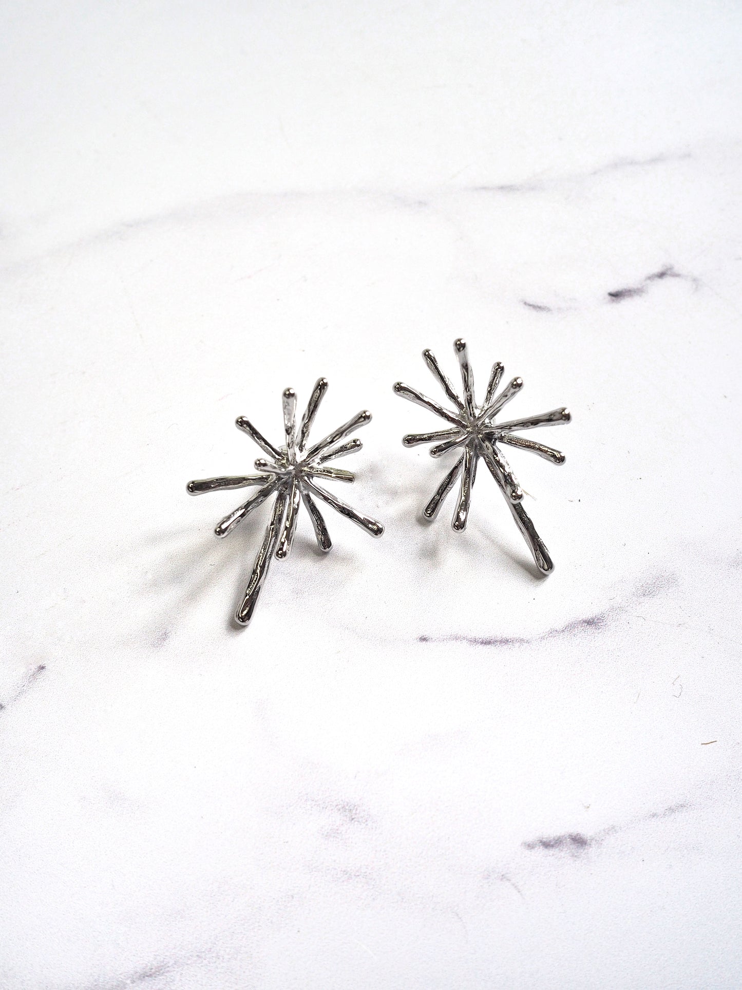 Pair of silver starburst earrings on a marble surface