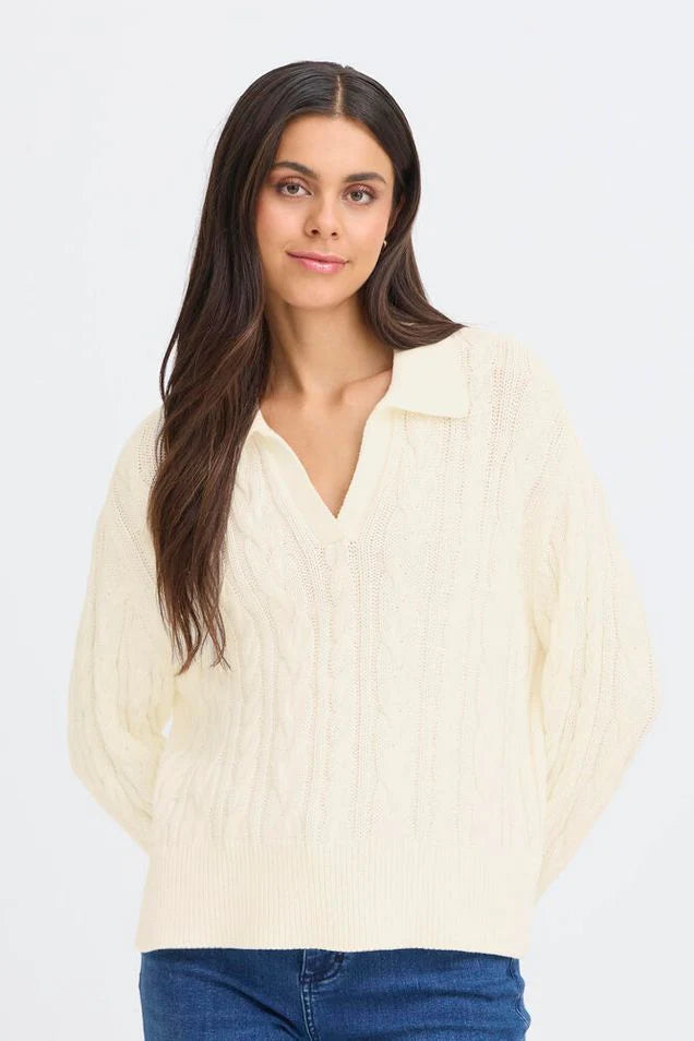 Woman wearing a cream cable knit pullover with blue jeans on a white background