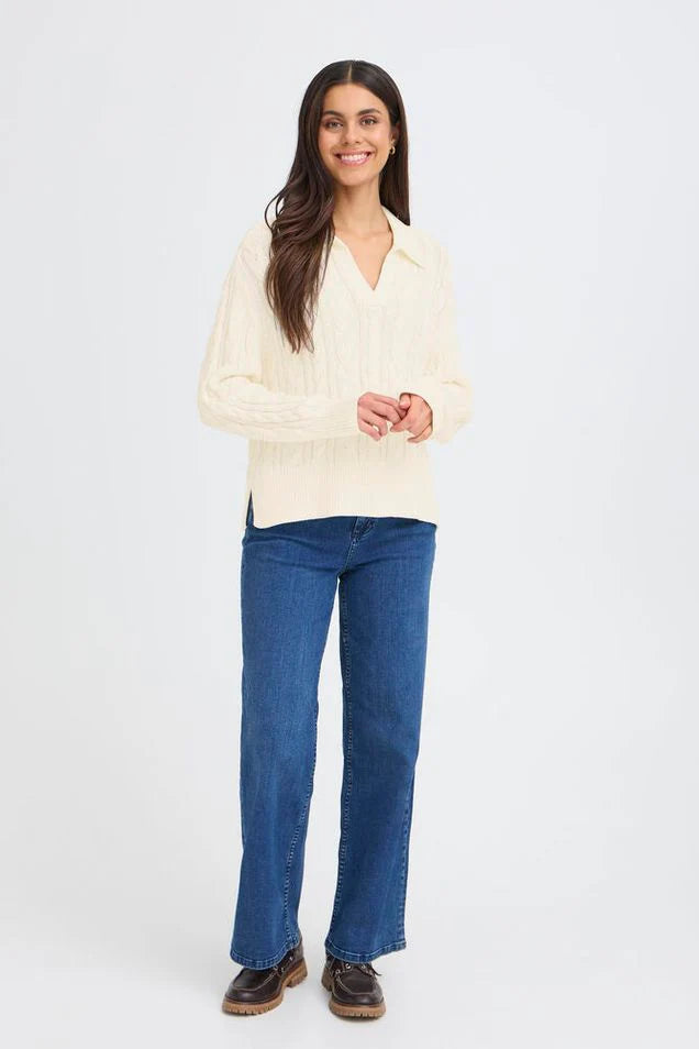 Woman wearing a cream cable knit pullover with blue jeans on a white background