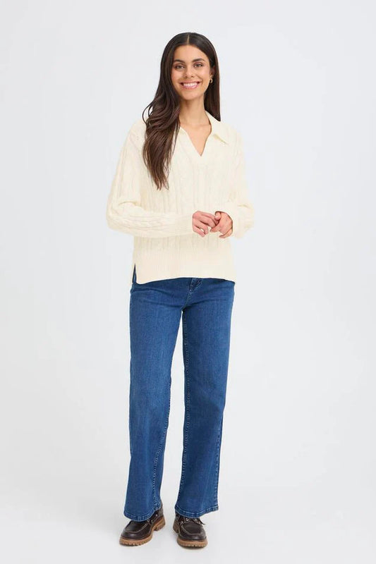 Woman wearing a cream cable knit pullover with blue jeans on a white background