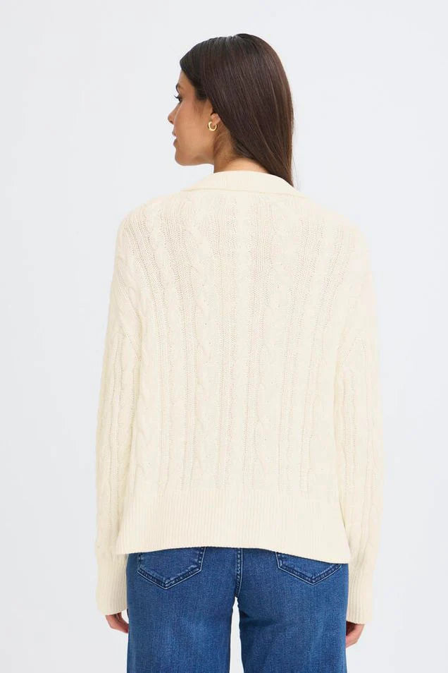 Woman wearing a cream cable knit pullover with blue jeans on a white background