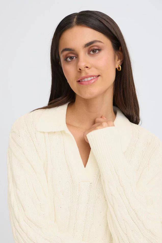 Woman wearing a cream cable knit pullover on a white background