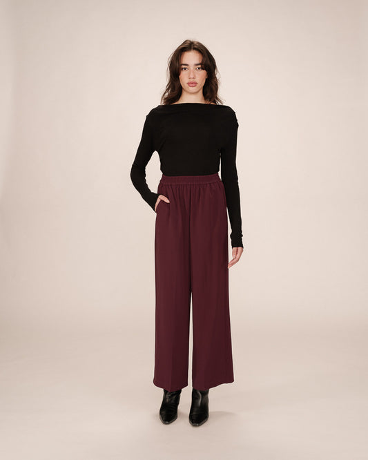 Woman wearing a black top and burgundy wide-leg pants on a beige background