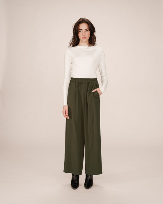 Woman wearing a white top and green wide-leg pants on a beige background
