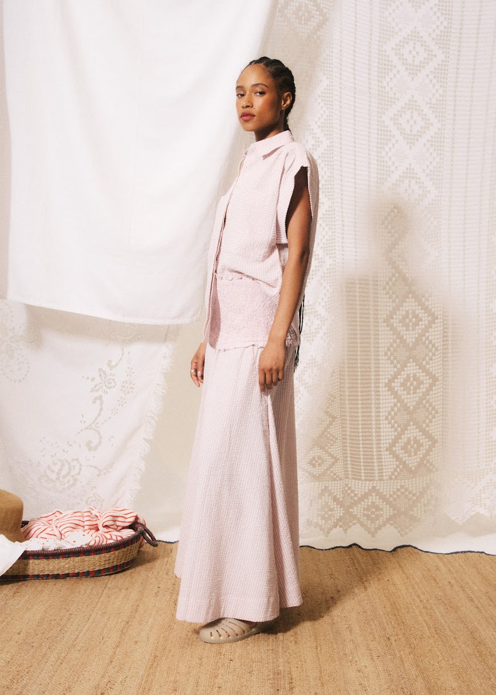 Woman in a light pink outfit standing against a textured white wall.