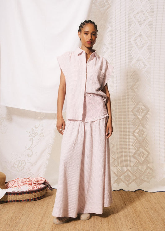 Woman wearing a light pink outfit standing in a room with a textured wall and basket.