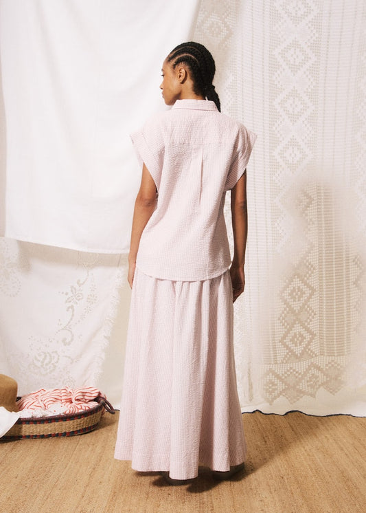 Woman in a light pink outfit standing in a room with white curtains.