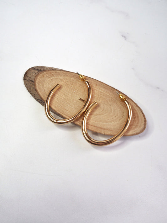 Gold hoop earrings on a wooden surface with a white background
