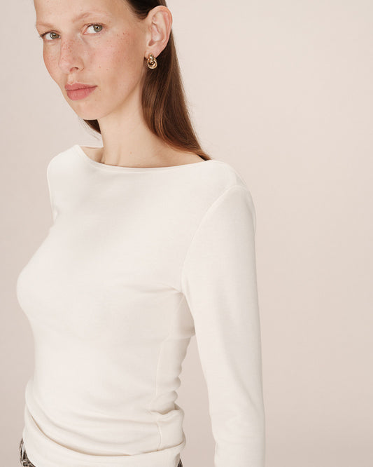 Woman wearing a white long sleeve t shirt against a plain background