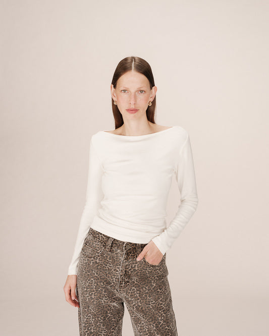 Woman wearing a white long-sleeve top and patterned pants on a beige background