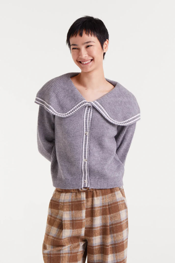 Person wearing a gray knitted cardigan with white trim on a white background