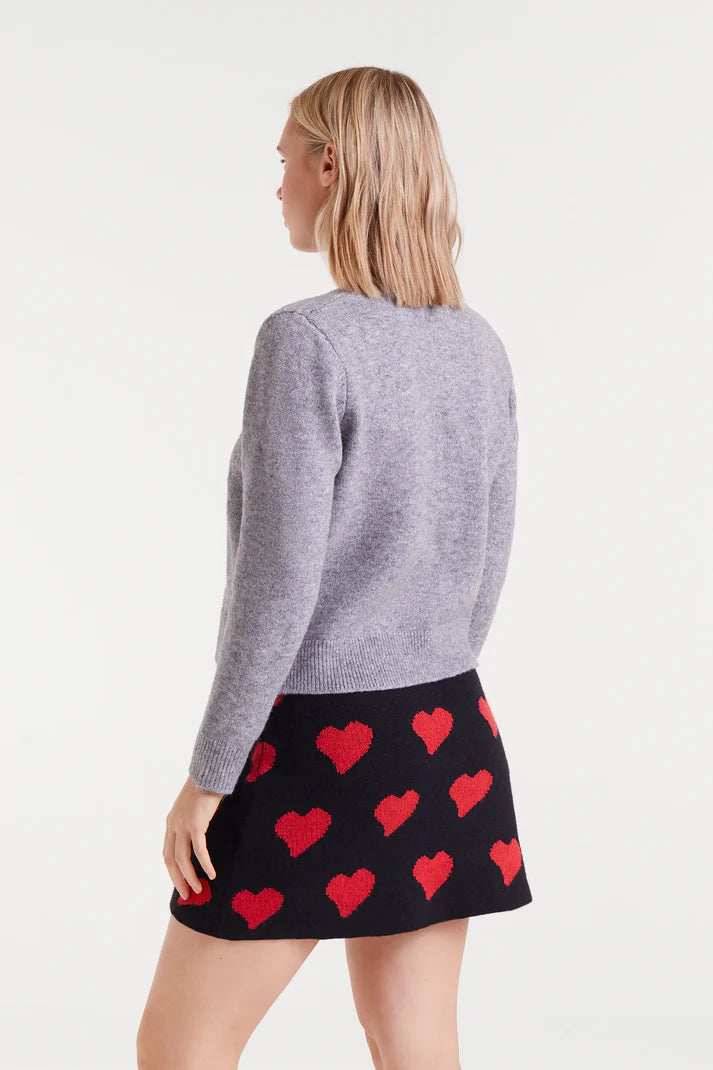 Woman wearing a gray sweater and black skirt with red heart pattern on a white background