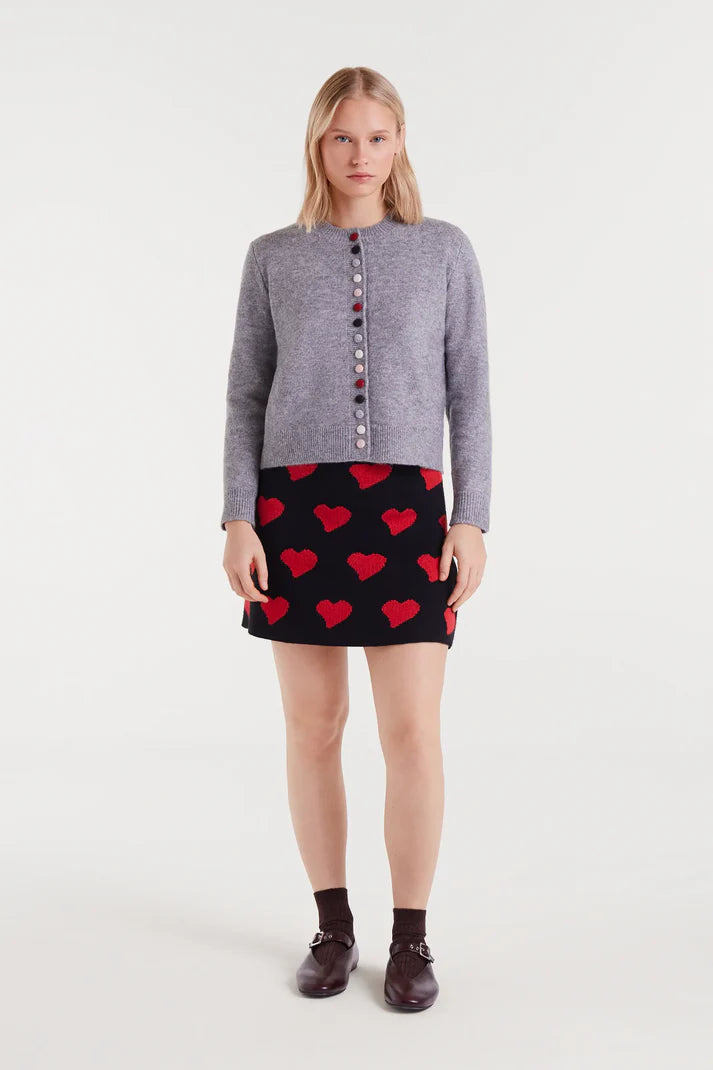 Woman wearing a gray sweater and red heart pattern skirt on a white background