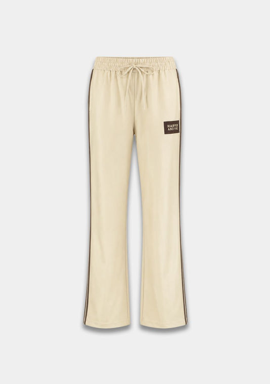 Cream-colored wide-leg sweatpants with dark brown side stripes and a small dark brown 'PASTRY CRAFTS' brand patch on the left thigh, shown against a light gray background.