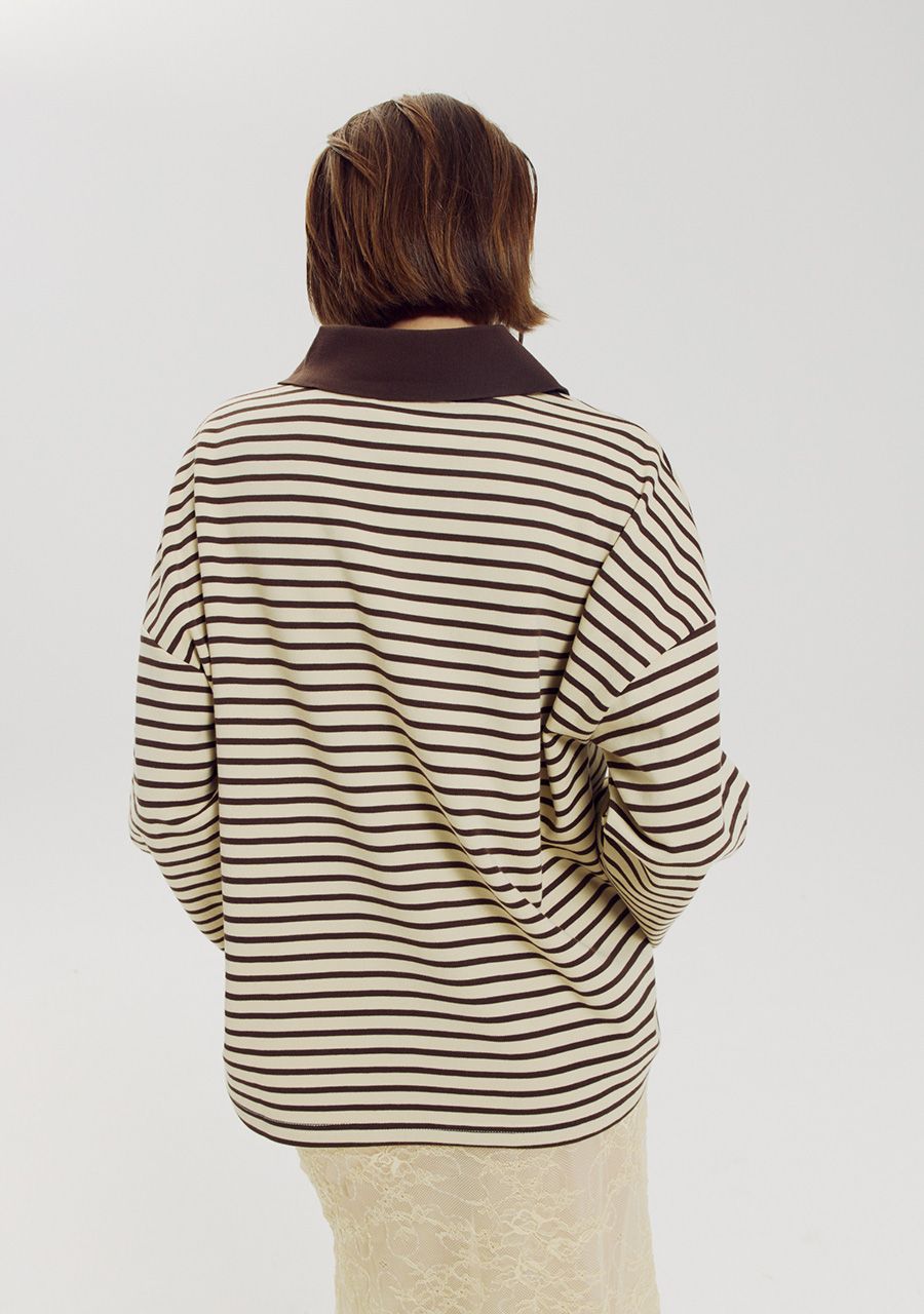 A person shown from the back wearing a cream and dark brown horizontally striped long-sleeve top with a solid dark brown collar, paired with a light beige skirt, against a plain light gray studio background.