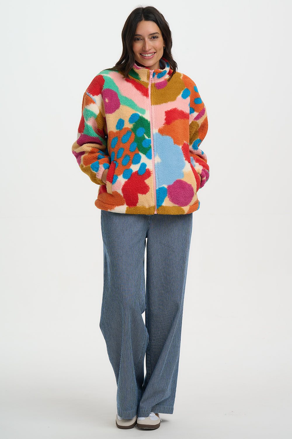 Woman wearing a colorful floral jacket and blue pants on a white background