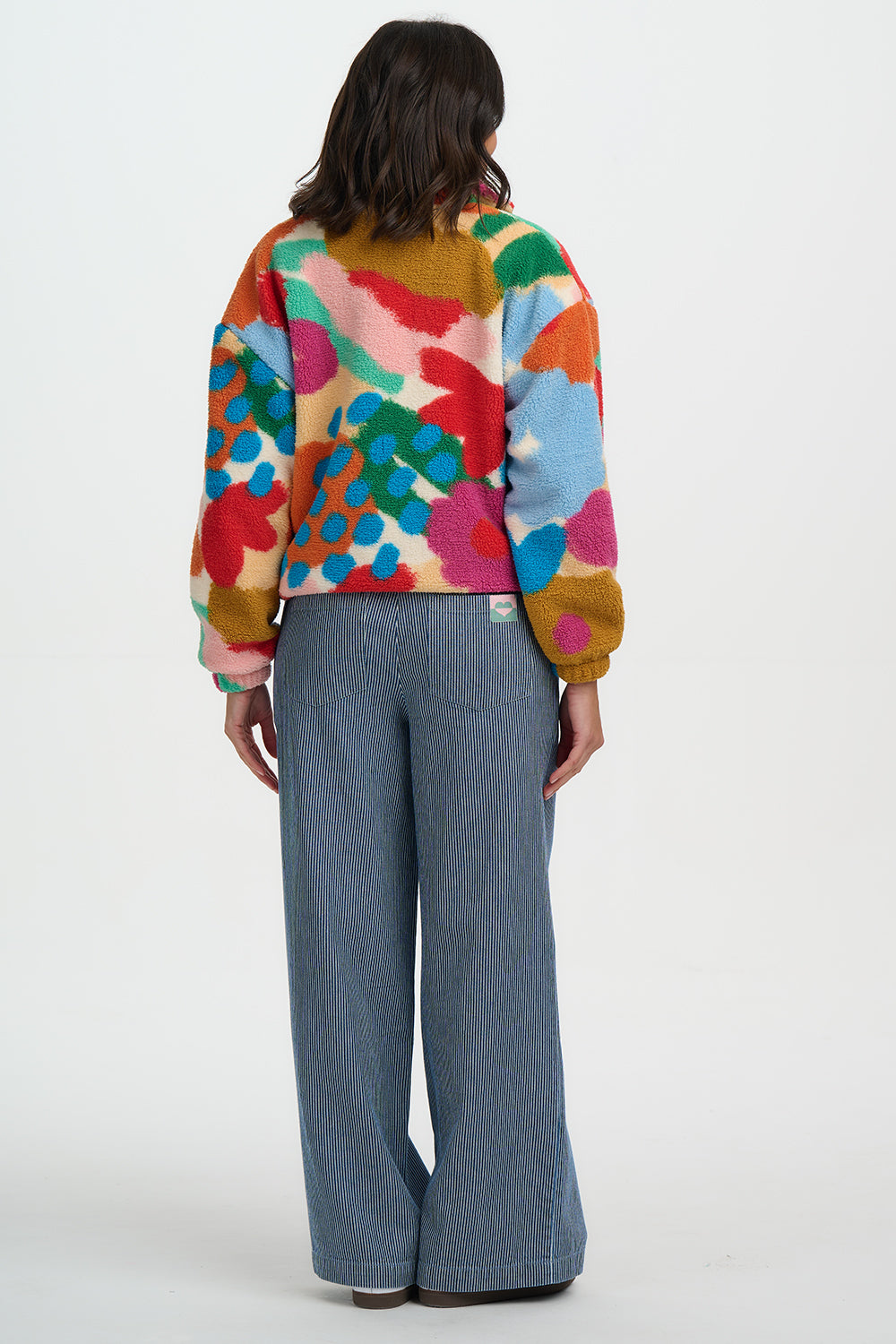Person wearing a colorful floral-patterned jacket and blue jeans on a white background