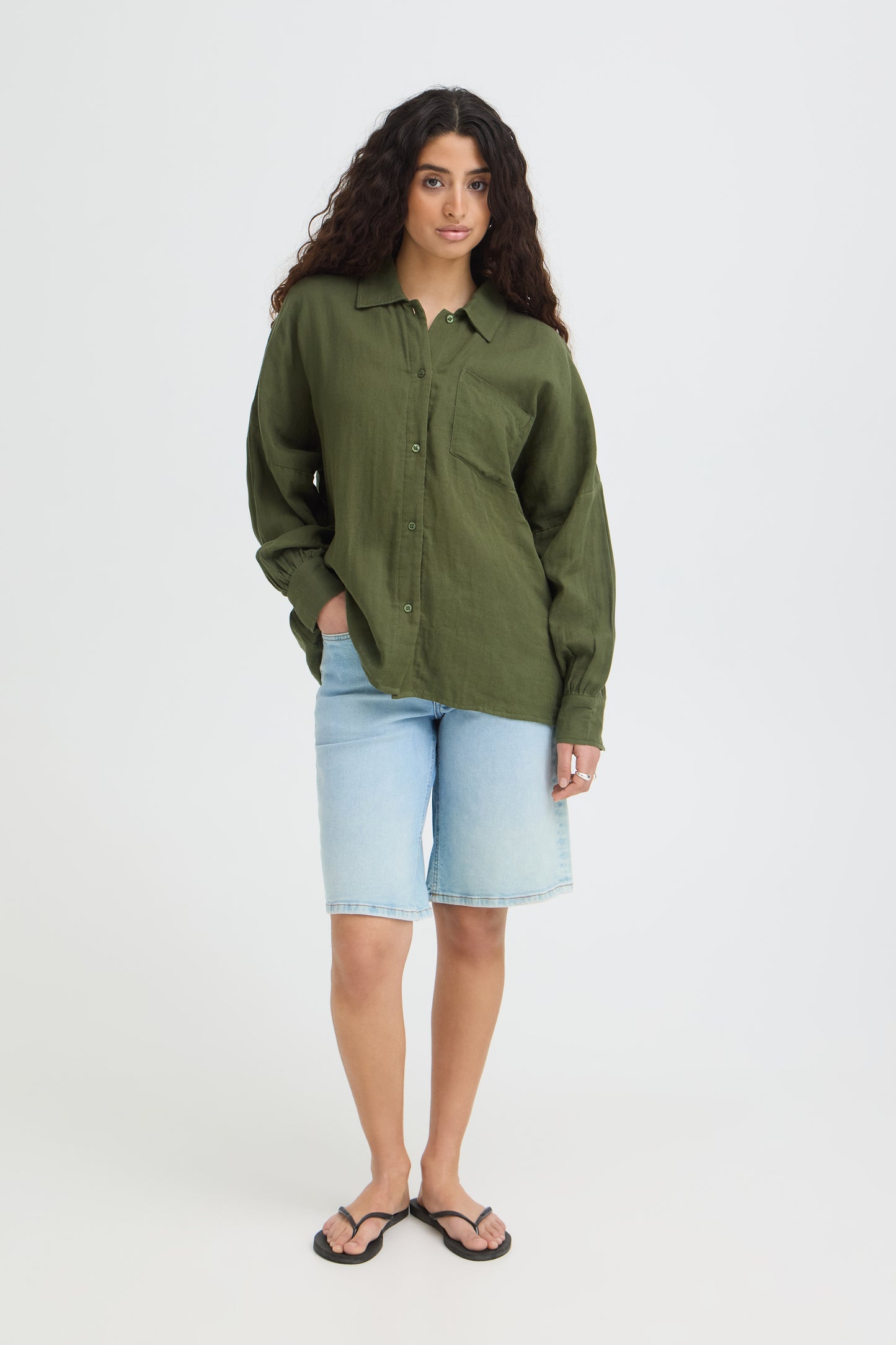 Woman wearing a green shirt and light blue shorts on a white background