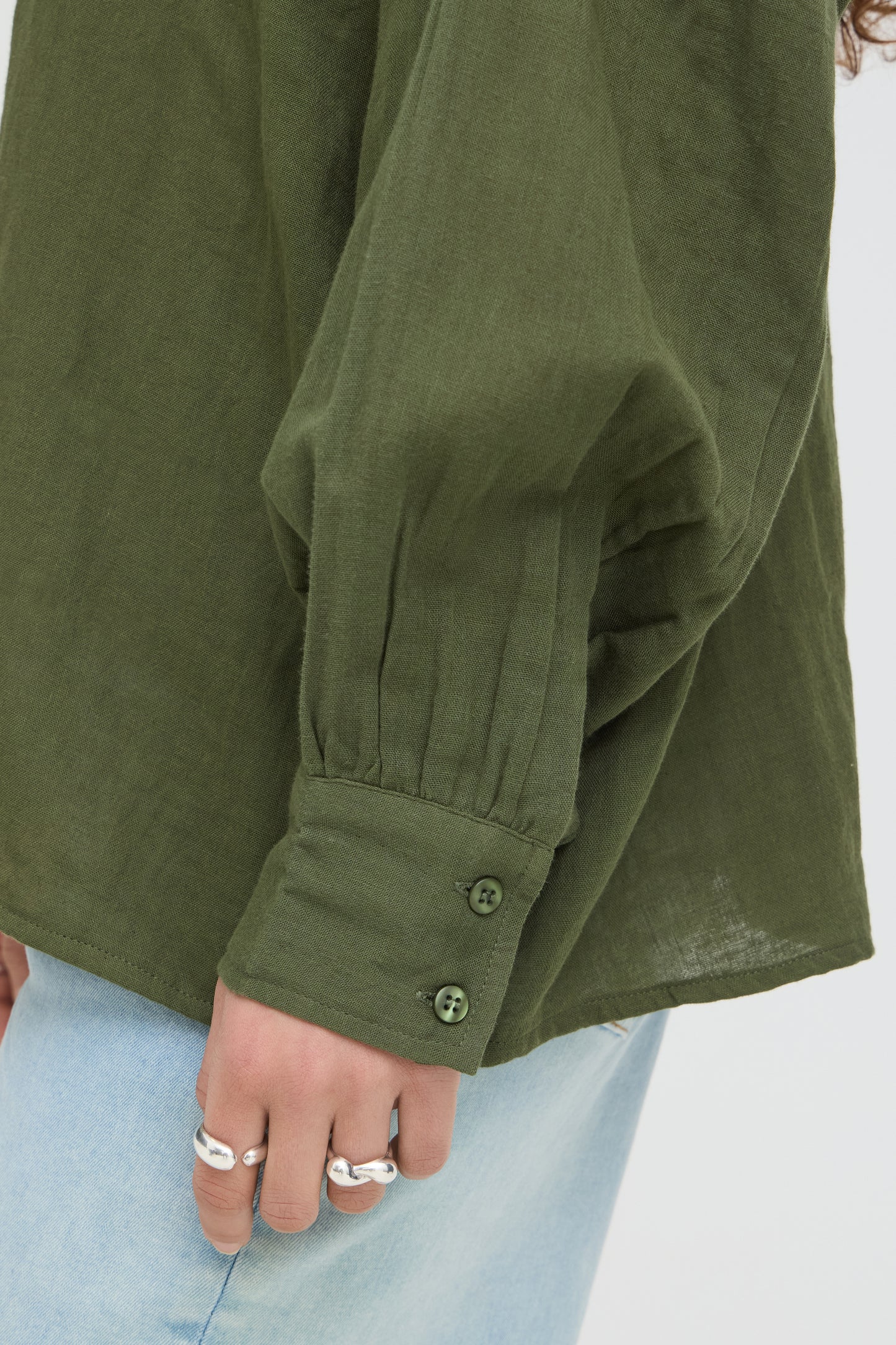 Close-up of a person wearing a green jacket with light blue jeans on a white background