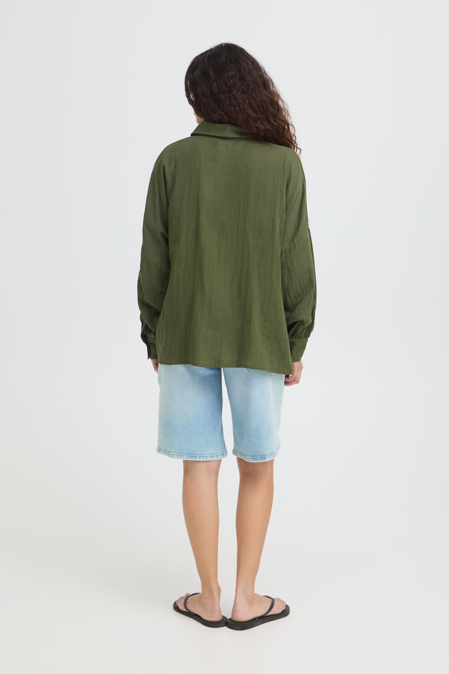 Person wearing a green jacket and light blue shorts on a white background
