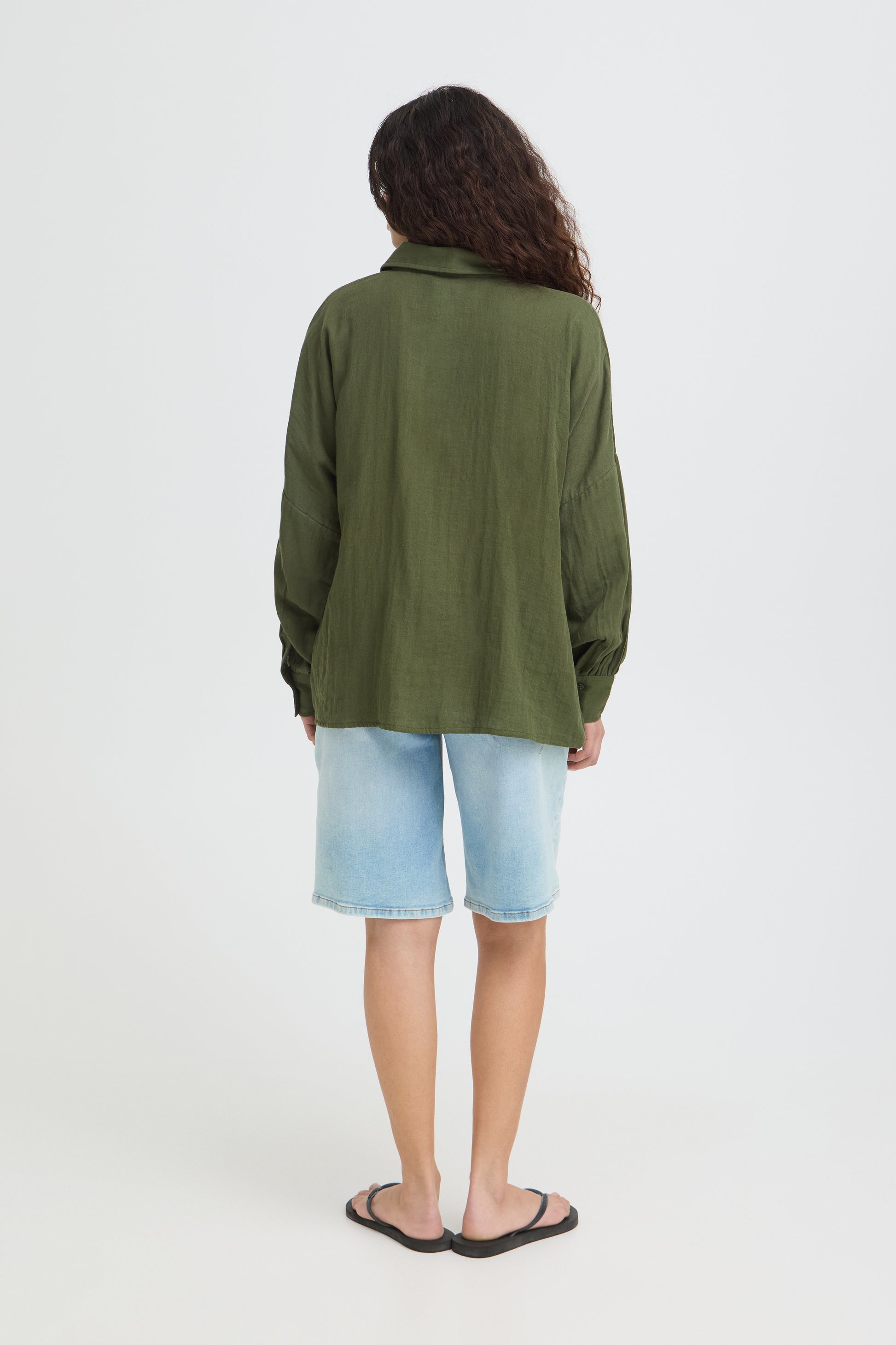 Person wearing a green jacket and light blue shorts on a white background
