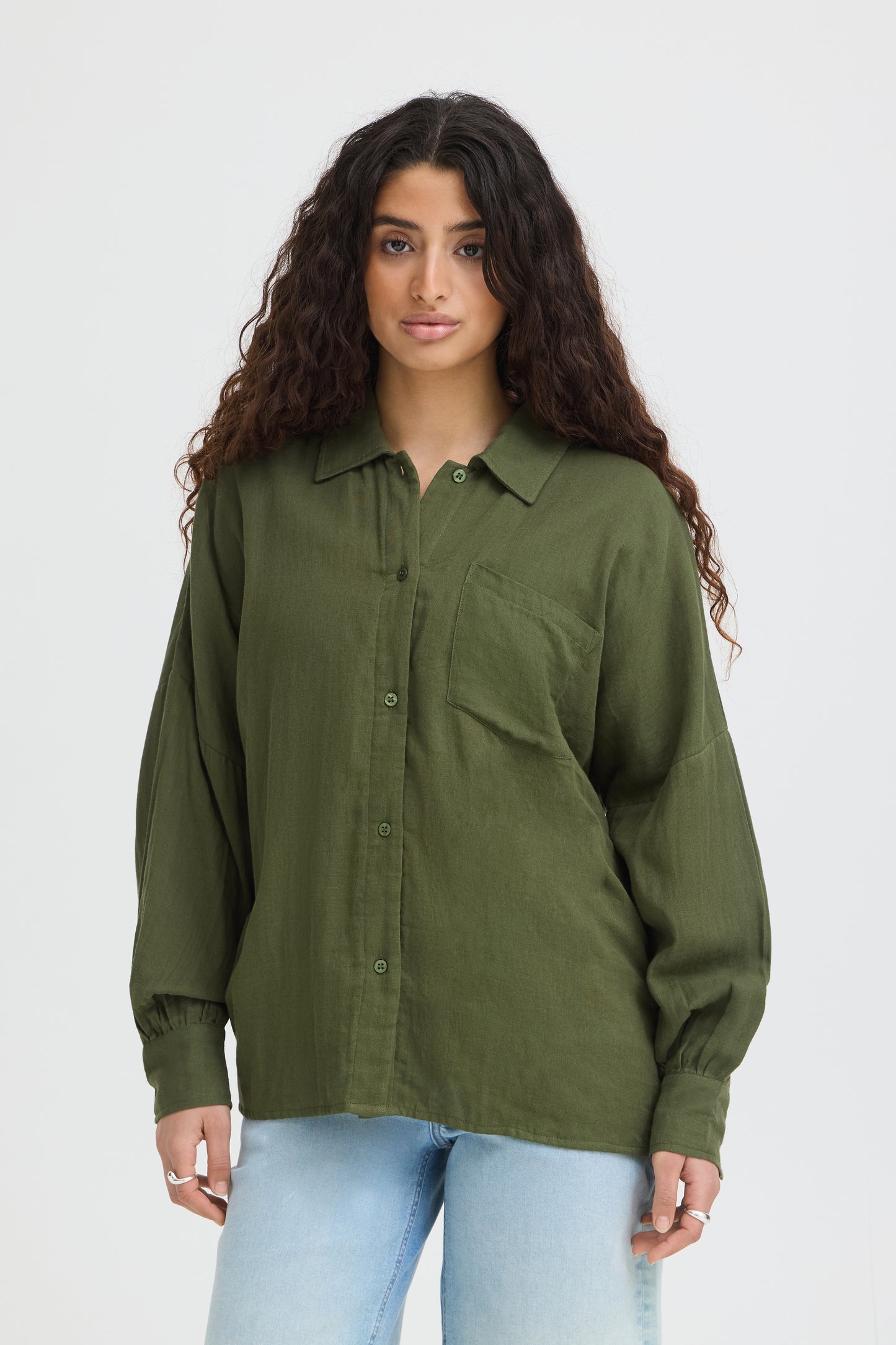 Woman wearing an olive green button-up shirt and light blue jeans on a white background