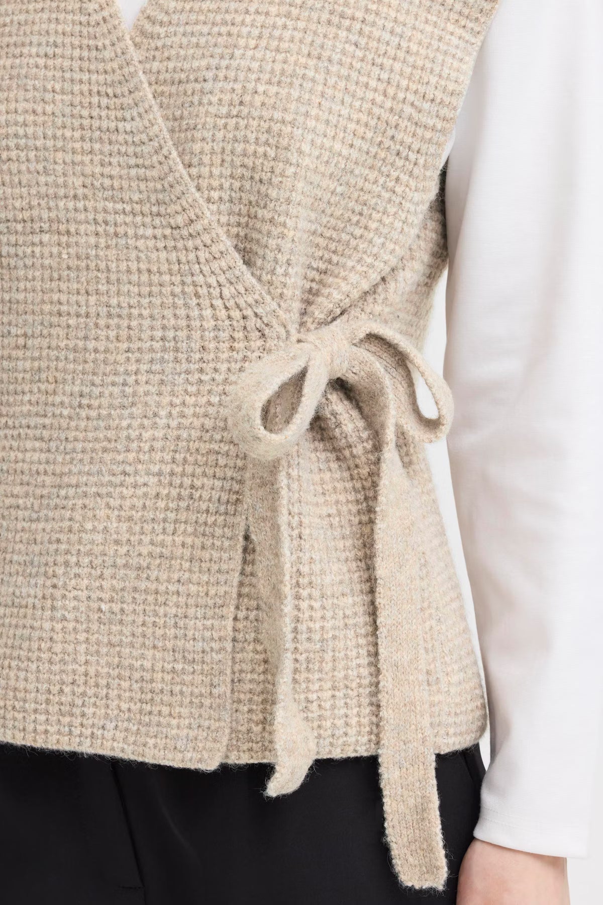 Beige knitted vest with a tie detail worn over a white shirt.