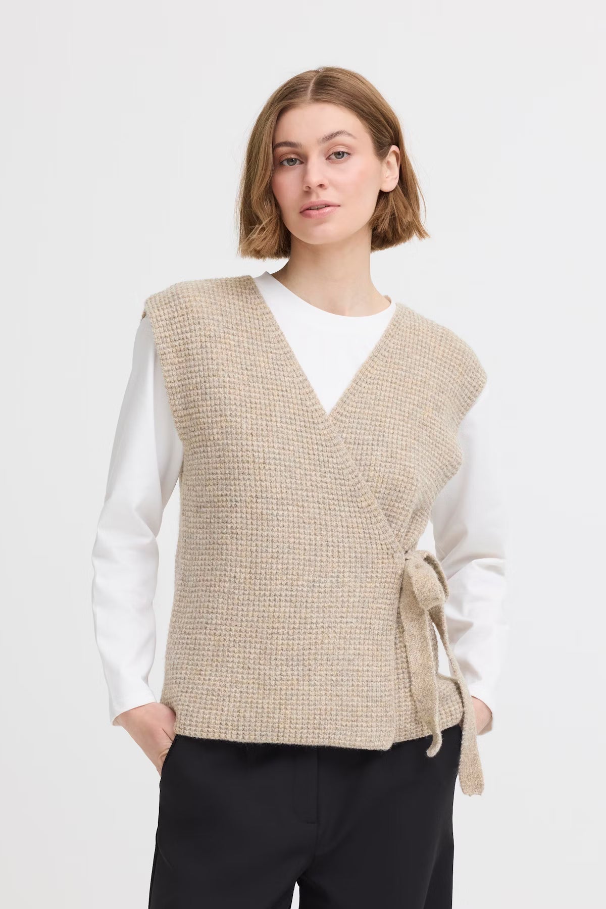 Woman wearing a beige knitted vest over a white shirt on a white background