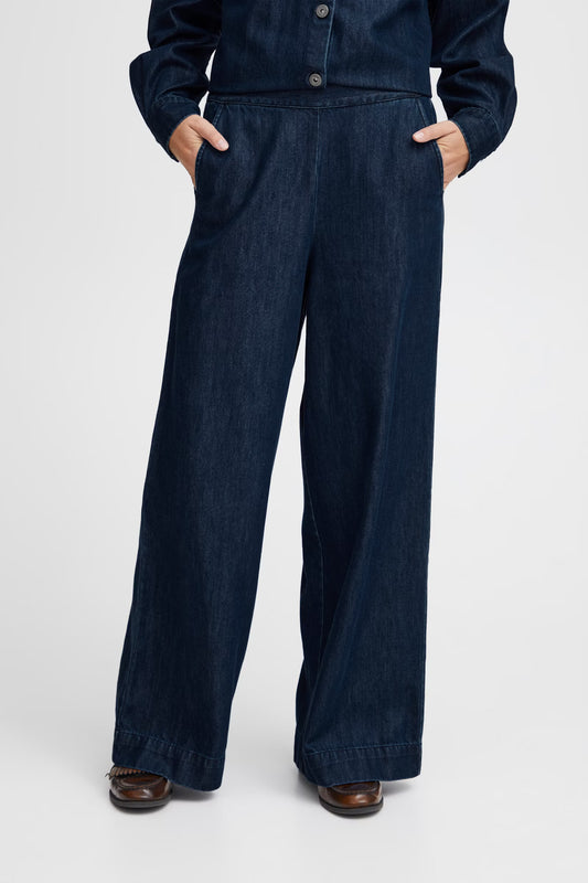 Person wearing a dark blue denim jumpsuit on a white background